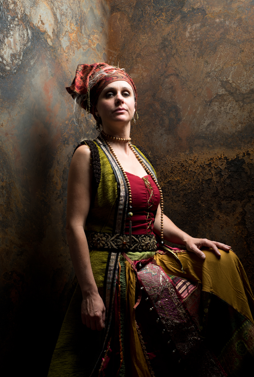 La conteuse est assise sur un tabouret haut, est habillé d'un costume chatoyant et elle regarde le public 