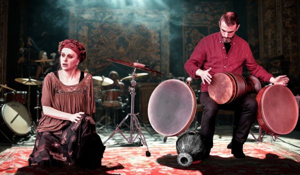 la conteuse est assise sur le tapis un turban dans la chevelure et le musicien joue des percussions iraniennes assis sur un tabouret à côté d'elle.