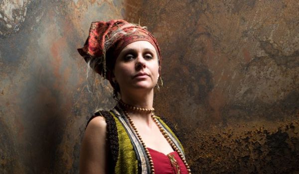 La conteuse est assise sur un tabouret haut, est habillé d'un costume chatoyant et elle regarde le public 