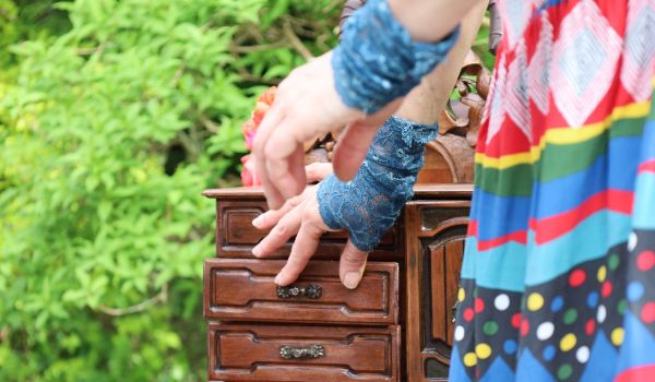 Des mains avec des mitaines en dentelles bleues ouvrent les tiroirs d'une armoire à graines rustique dans un jardin de verdure. 
