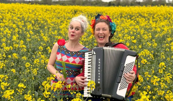 Au milieu d'un champs de colza jaune lumineux, Stephanie Jancar, en robe de clown, tulipe rouge dans la main et Clémence Vandaele chanteuse, fleurs dans les cheveux, jouant de l' accordéon, rayonnent de joie. 